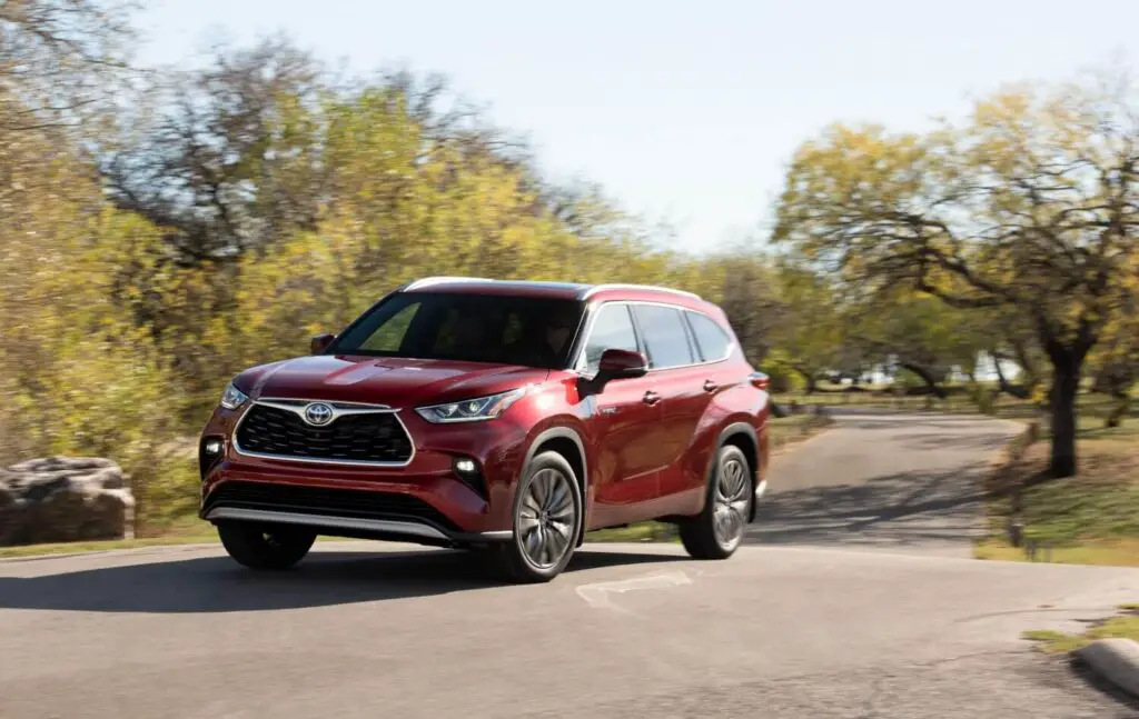 The 2021 Toyota Highlander driving on a windy, paved road with trees on either side.