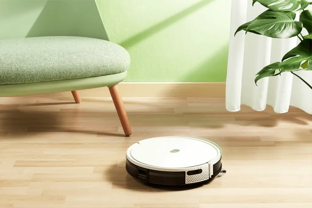 The Yeedi K650 Robotic Vacuum in a beautiful green room by a chair and a plant.