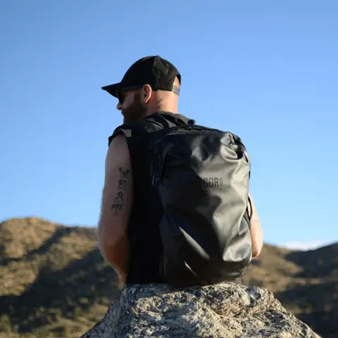A man sitting on a large boulder carrying the Island Hopper bag from COR surf.