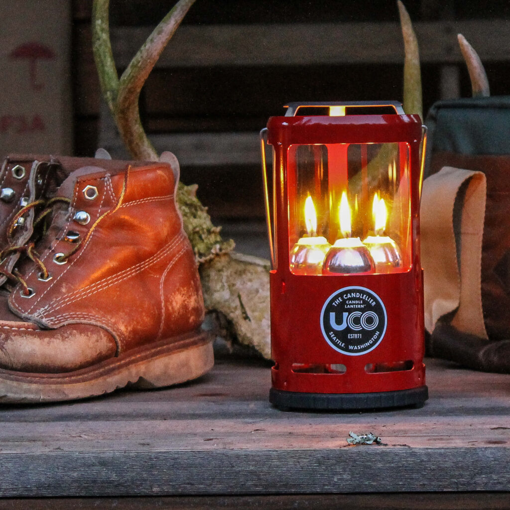 The red UCO Candlelier sitting on a porch by some deer antlers and work boots.