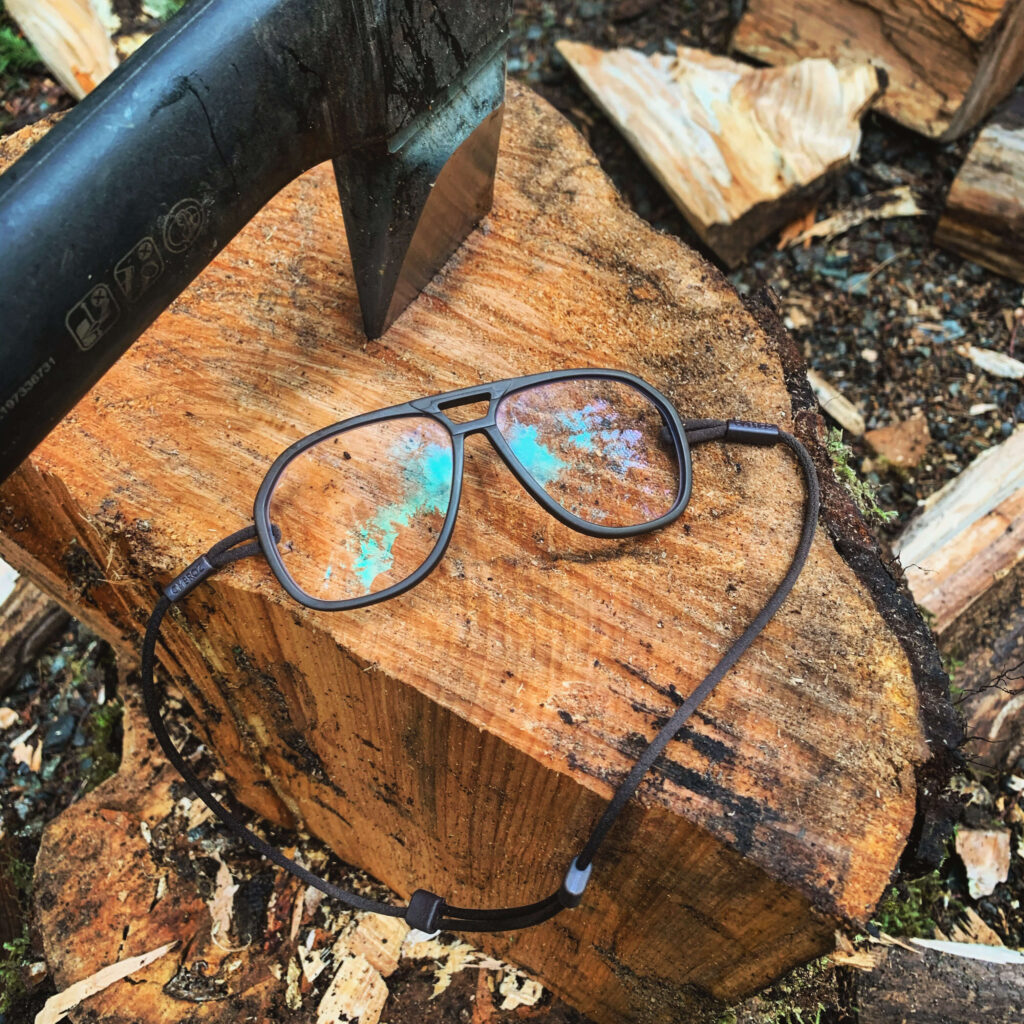 The special clear blue blockers from Ombraz laying out on a log next to an axe that has been stuck into the wood.