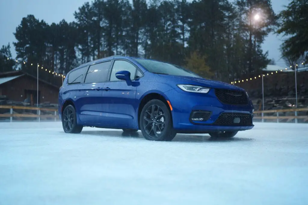 A blue Chrysler Pacifica on an ice rink while it's raining.