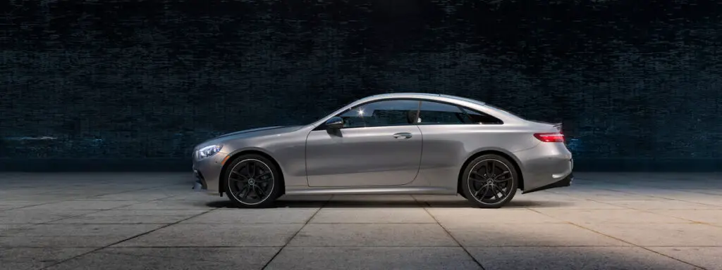 A silver 2021 Mercedes-Benz E 450 AMG Coupe, which contains the new heat map feature that all these vehicles can brag about, on a paved area in the dark.