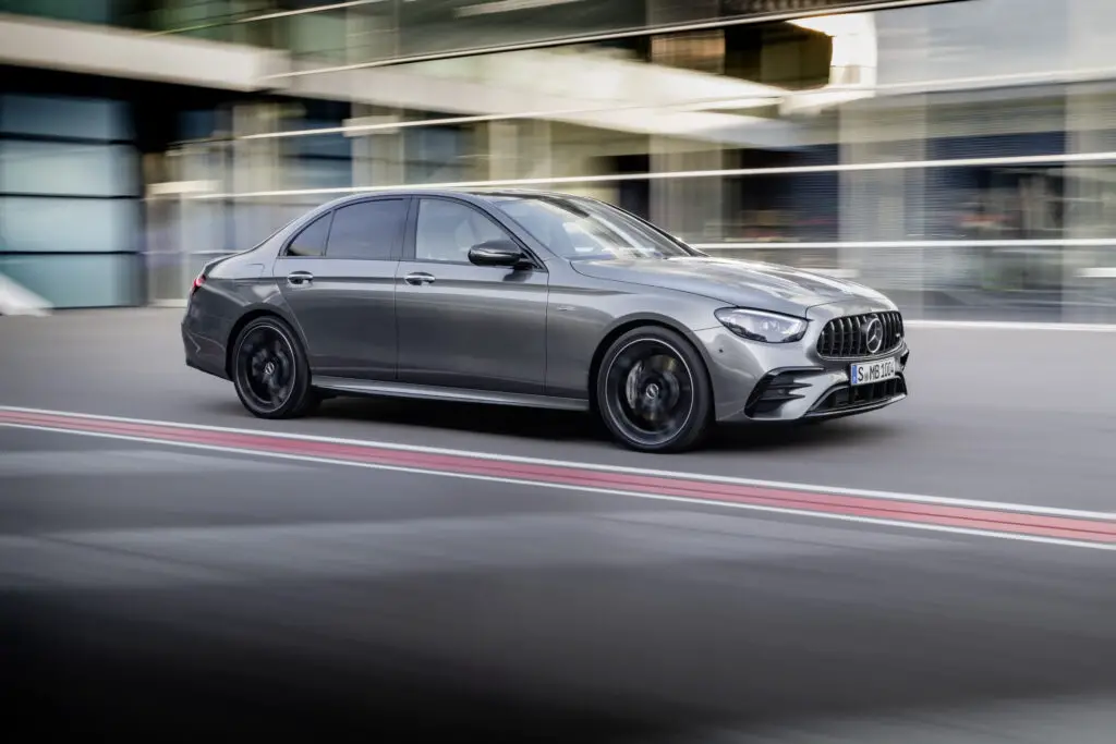 The 2021 Mercedes-Benz AMG E 53 driving quickly down a city road using its unique steering wheel.