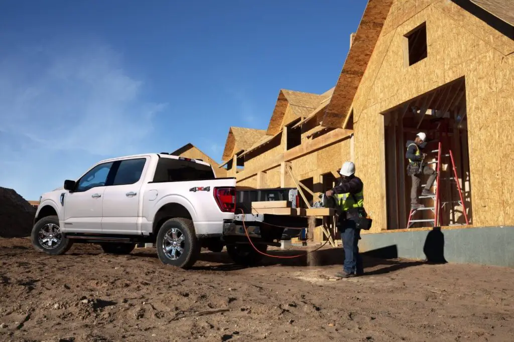 The Ford 2021 F-150 4x4 Supercrew XLT on a construction site with the back loaded with lumber and using its generator to power a saw.