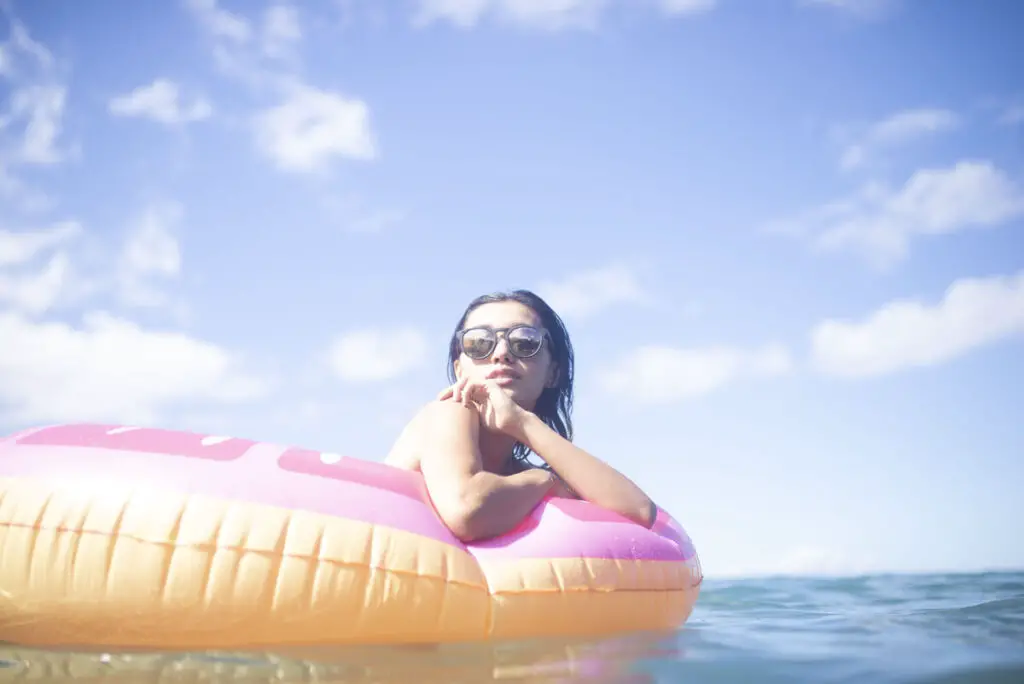 A woman wearing her Opus LL sunglasses by Dragon Alliance while on an inflatable floaty.