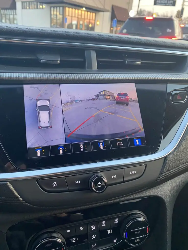 A backup camera view as well as an overhead view side by side shown on screen while backing out of a parking space.