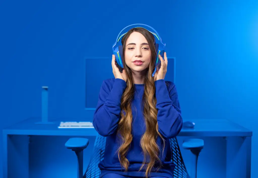A woman wearing her Logitech G733 gaming headset in a room that is completely blue (even the chair, desk, and computer).