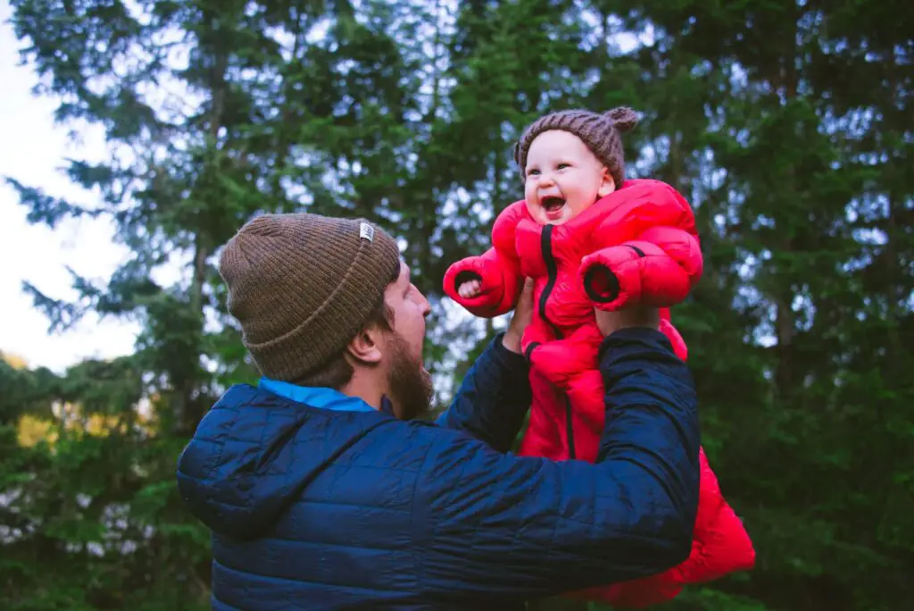 A dad holding his baby that is cuddled up and smiling inside the Morrison Outdoors sleeping bag.
