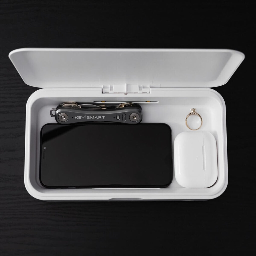 The CleanTray UV Sterilization Case holding a phone, pocket knife, AirPods, and wedding ring.