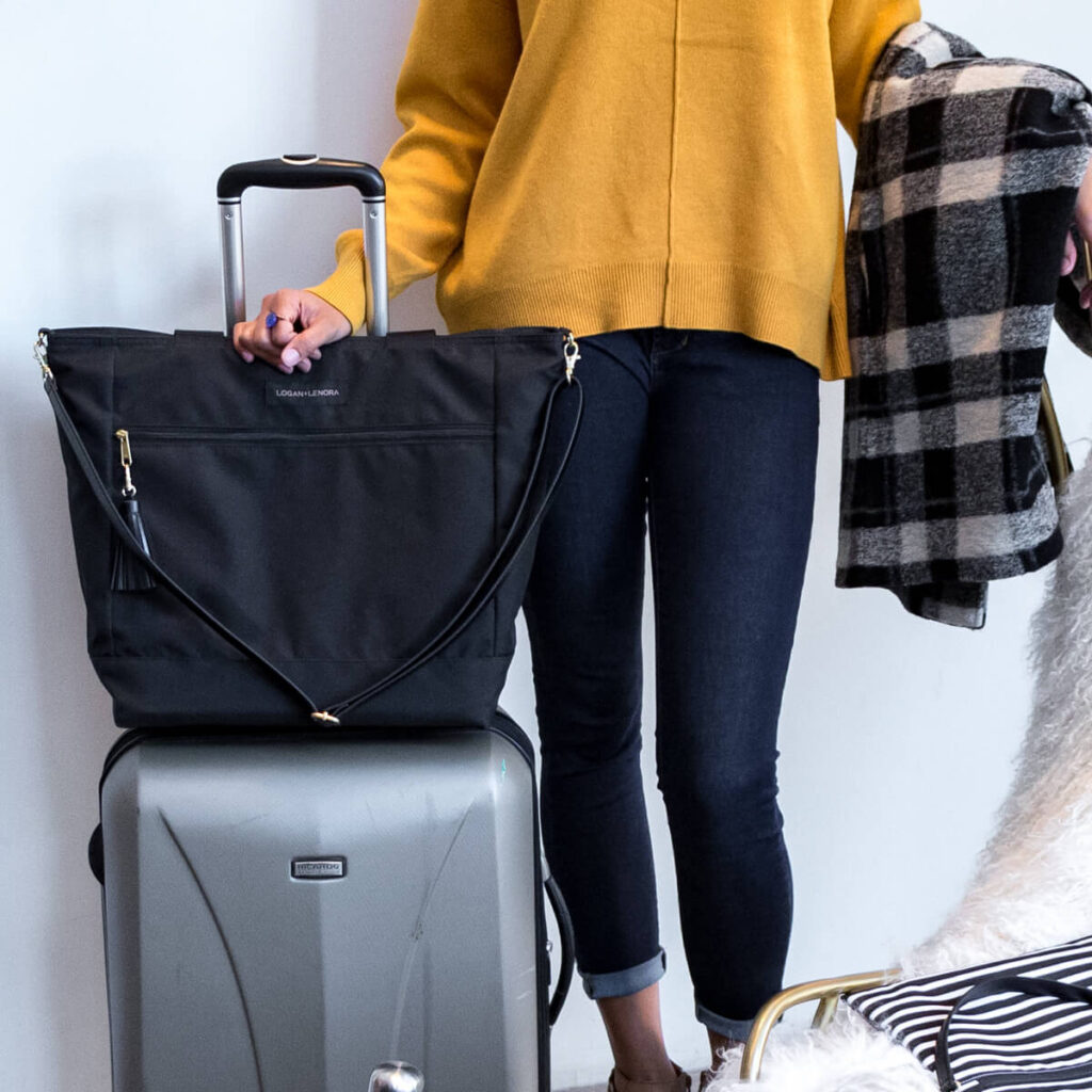 A woman ready for a trip with her suitcase and her Logan + Lenora Weekender bag.