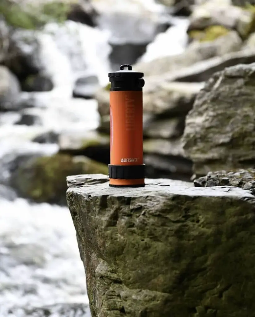 An orange LifeSaver Liberty Bottle sitting on a large stone next to a waterfall and stream.
