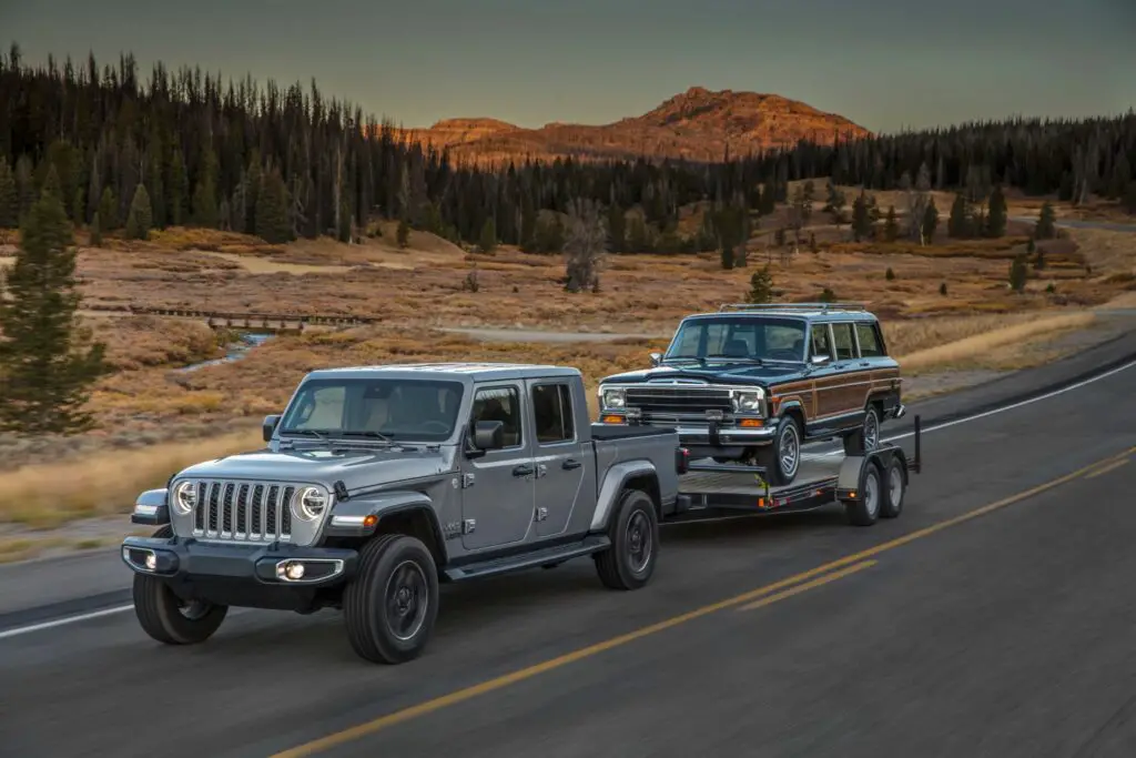 The 2021 Jeep Gladiator Overland Pickup on a mountain road trailering another, old car behind it.