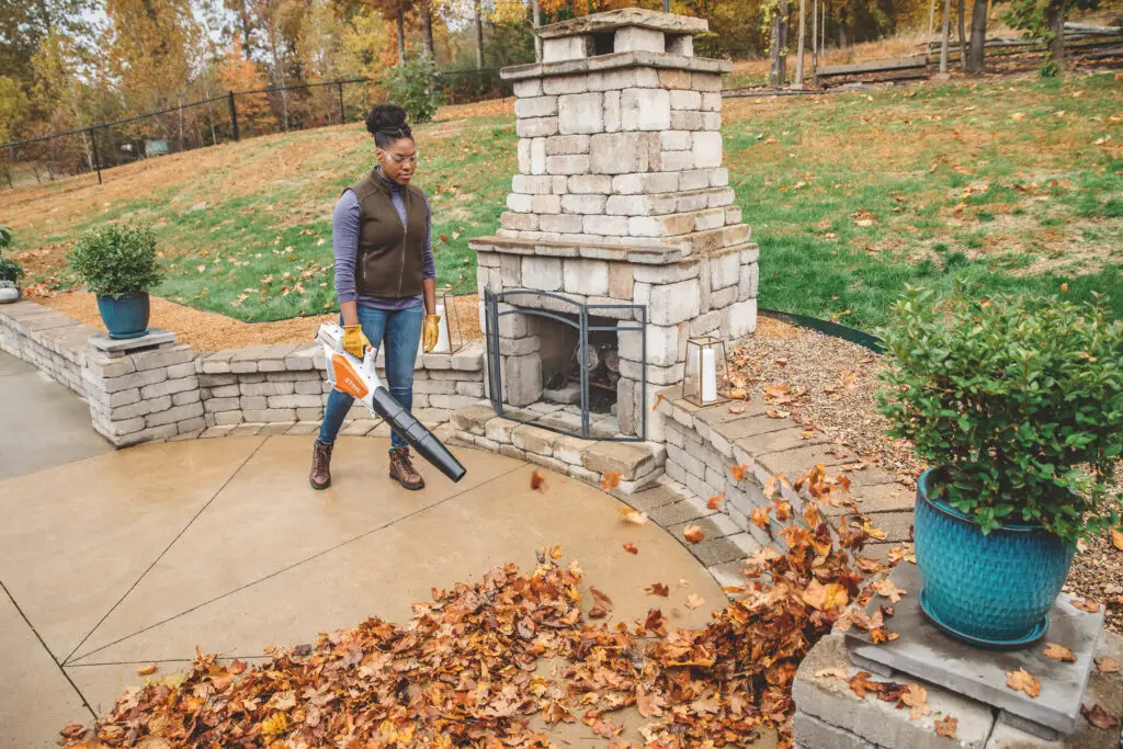 A woman cleaning up her yard from fall leaves by using her Stihl BGA 56 Leaf Blower.