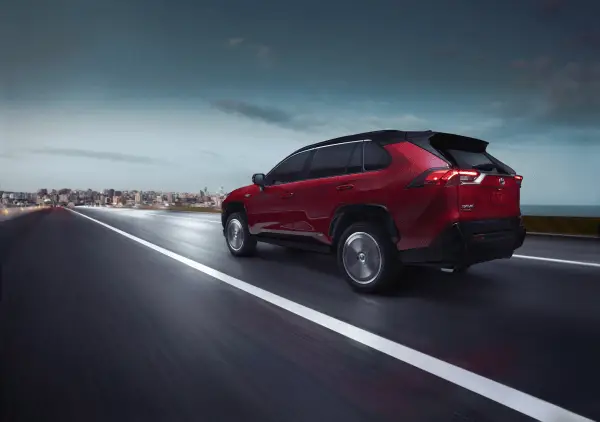 A red 2021 Toyota RAV4 Prime XSE Premium driving down a road into a city.