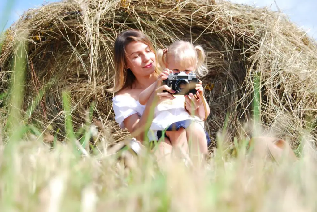 A mom and her daughter sitting by a hay bale taking a photo for their PhotoShare.