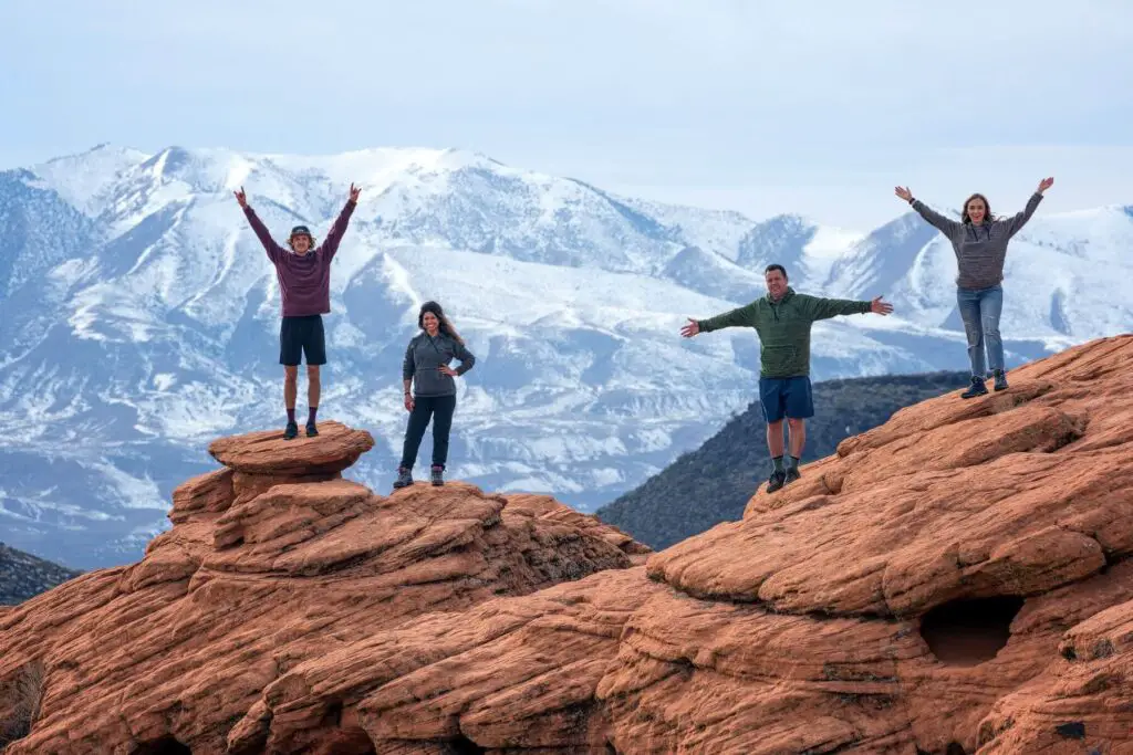 Two men and two women on the top of a large rock formation by some beautiful mountains as they wear their CoalaTree Evolution Hoodies.