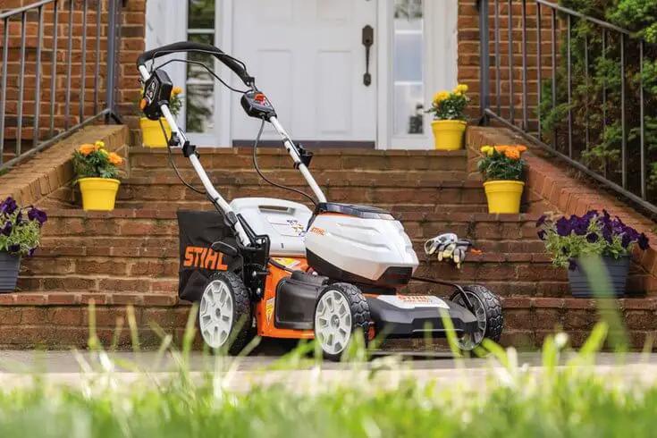 The Stihl RMA 460 V, a battery-powered mower, sitting on the porch of a house with a beautiful yard.