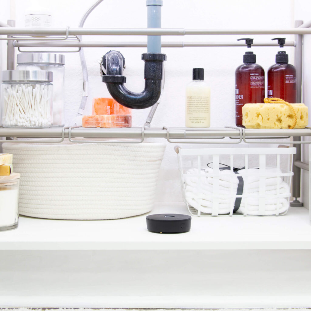The Phyn water sensor in a cozy cabinet storage cabinet with lots of cleaning supplies.