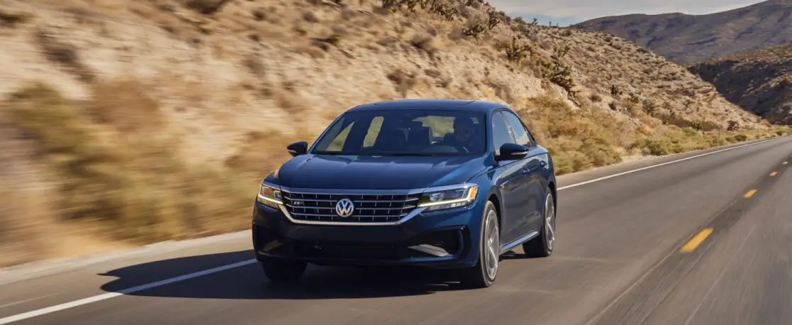 The 2021 VW Passat R-Line driving on a highway next to a grassy mountain.
